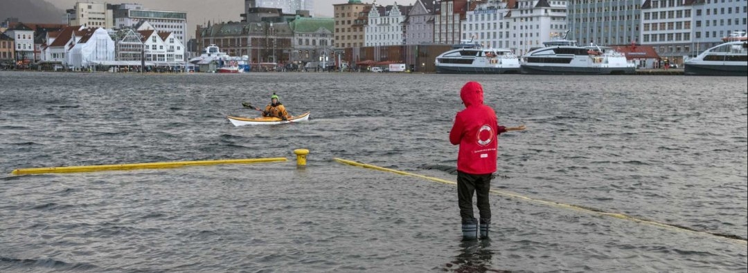 Bilde av oversvømmelse på Bryggen i Bergen. En mann står i gummistøvler på oversvømmet kaikant.