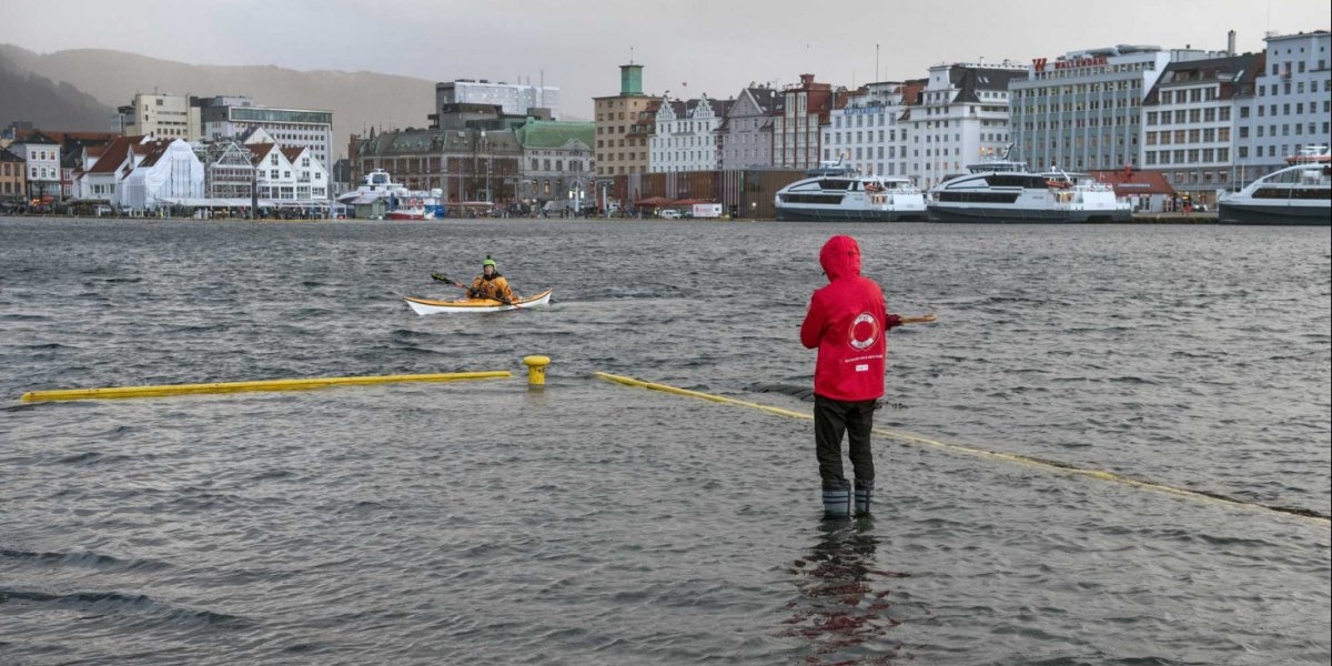 Bilde av mann med gummistøvler som står på oversvømmet kaikant.